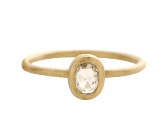 May include: A gold ring with an oval-shaped, clear diamond center stone. The band and setting have a matte finish. The ring is a simple, elegant design, suitable for everyday wear or special occasions.