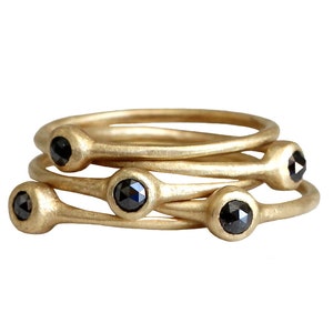 May include: Set of four gold rings with black diamonds. Each ring has a single black diamond set in a smooth gold band.