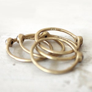May include: Four gold rings with small black stones set in the center of each ring. The rings are stacked on top of each other.
