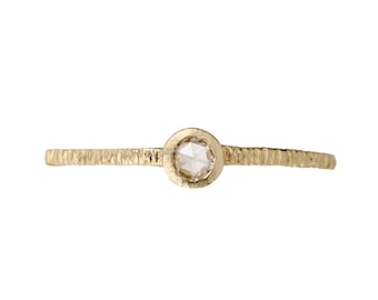 May include: A delicate gold ring with a textured band and a small, clear diamond.