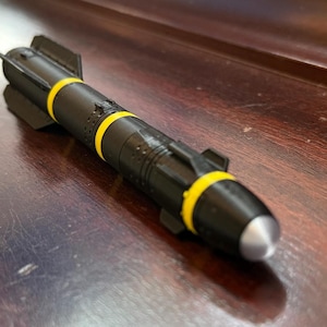 May include: A black model missile with yellow bands and a silver tip. The missile has fins and other detailed features. It is resting on a dark wooden surface.
