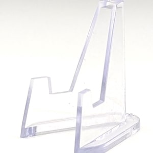 May include: A clear, plastic display stand with a triangular shape. The stand has a flat base and a support arm that angles upward. The stand is designed to hold and display small items.