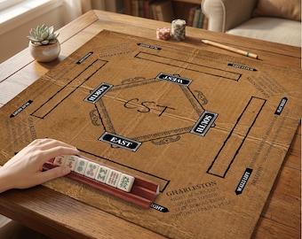 May include: A brown Mahjong game mat featuring a central diamond design with the letters CST, labelled North, South, East, and West, and printed instructions for Charleston play. A wooden tile rack holds several white Mahjong tiles with red and green symbols.