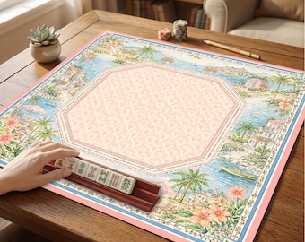 Puede incluir: Un tapete de mahjong cuadrado con un paisaje costero de palmeras, flores y edificios que rodea una zona central octogonal con estampado rosa. Un soporte de madera sostiene cinco fichas de mahjong con caracteres chinos.