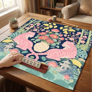 May include: A square mahjong mat featuring a dark blue background with two pink tigers, a central vase of pink lotus flowers, yellow ginkgo leaves, bamboo stalks, and stone lanterns. A wooden tile rack holds mahjong tiles with Chinese characters.