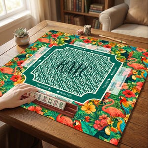May include: A square mahjong mat featuring a vibrant tropical pattern with pink flamingos, colorful parrots, toucans, and hibiscus flowers. The center has a dark green square with a white Greek key border and the handwritten text HMC.