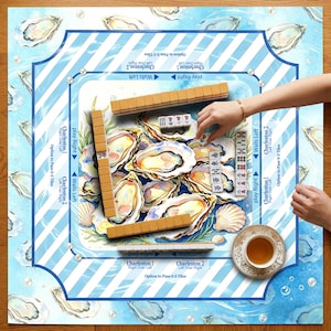 May include: A Mahjong game set with oyster shell and ocean wave design. The game board features a blue and white striped border with oyster illustrations. Wooden tiles and a teacup are visible, with hands arranging the tiles. The game is set on a wooden surface.