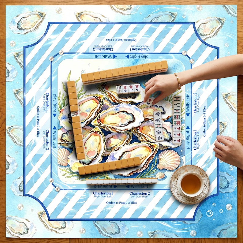 May include: A Mahjong game set with oyster shell and ocean wave design. The game board features a blue and white striped border with oyster illustrations. Wooden tiles and a teacup are visible, with hands arranging the tiles. The game is set on a wooden surface.