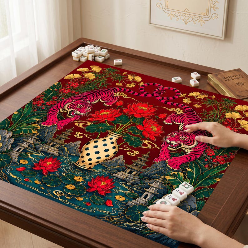 May include: A square mahjong mat featuring a deep red background with two pink tigers, a central cream-colored vase with black dots, red lotus flowers, green foliage, and traditional pagoda structures. White mahjong tiles are scattered on the mat.