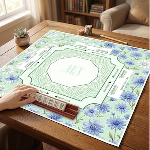 May include: A square mahjong mat featuring a light green background with a blue and white floral pattern. The center has an octagonal design with the letters MT. The mat includes printed game instructions and a wooden rack with mahjong tiles.