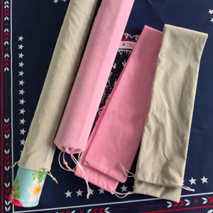 May include: Four long, cylindrical fabric storage sleeves with drawstring closures at the bottom. Two sleeves are beige and two are light pink. One beige sleeve partially reveals a light blue patterned item with white floral designs inside.