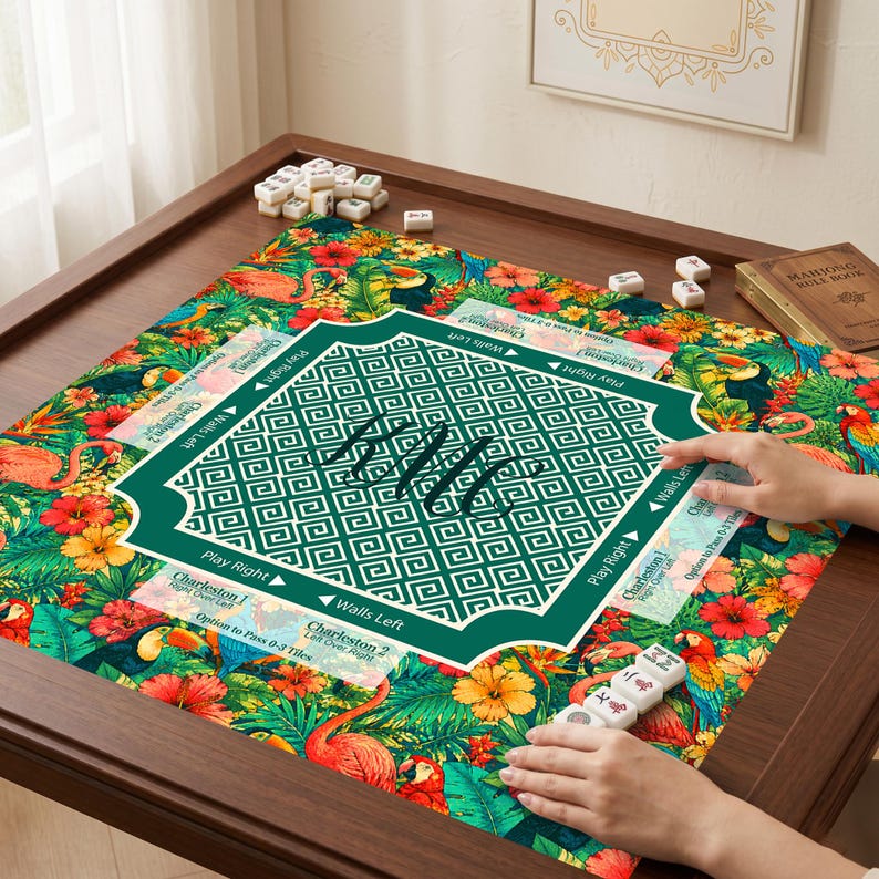 May include: A square mahjong mat featuring a vibrant tropical pattern with flamingos, toucans, parrots, and hibiscus flowers. The center has a dark green square with a white Greek key border and the text "Charleston" with directional arrows.
