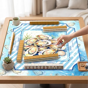 May include: A wooden Mahjong table with a blue and white oyster-themed playing surface. The game is set up with tiles and accessories. The table is surrounded by wooden trim. A hand is reaching for a tile.