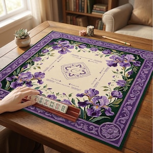 Puede incluir: Un tapete de Mahjong cuadrado con un centro color crema con instrucciones de juego impresas y un borde floral morado decorativo con ilustraciones de lirios. Un soporte de madera sostiene varias fichas de Mahjong con caracteres chinos.
