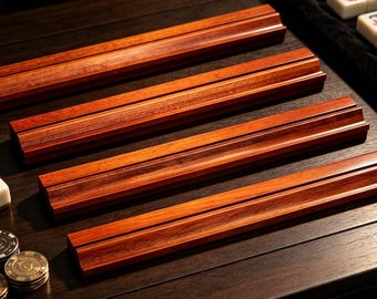 Puede incluir: Cuatro soportes rectangulares de madera para fichas de mahjong con un acabado en tono marrón rojizo intenso. Cada soporte presenta una ranura horizontal larga diseñada para mantener las fichas de juego en posición vertical y alineadas.