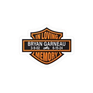 May include: A sticker with a black and orange design. The sticker reads "IN LOVING MEMORY" and includes the name "BRYAN GARNEAU" with dates and a motorcycle graphic. The sticker has a shield shape.