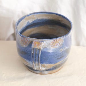 Puede incluir: Taza de cerámica hecha a mano con una combinación de azul, beige y azul oscuro. La taza tiene un asa y está decorada con diseños de conchas marinas. Adecuada para bebidas frías o calientes.