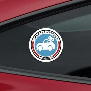 Puede incluir: Una pegatina circular con un centro azul claro y la silueta blanca de un coche con una llave de cuerda en el techo. El texto "SAVE THE MANUALS" y "HERITAGE" está impreso en negro sobre el borde blanco, con arcos rojos y negros.