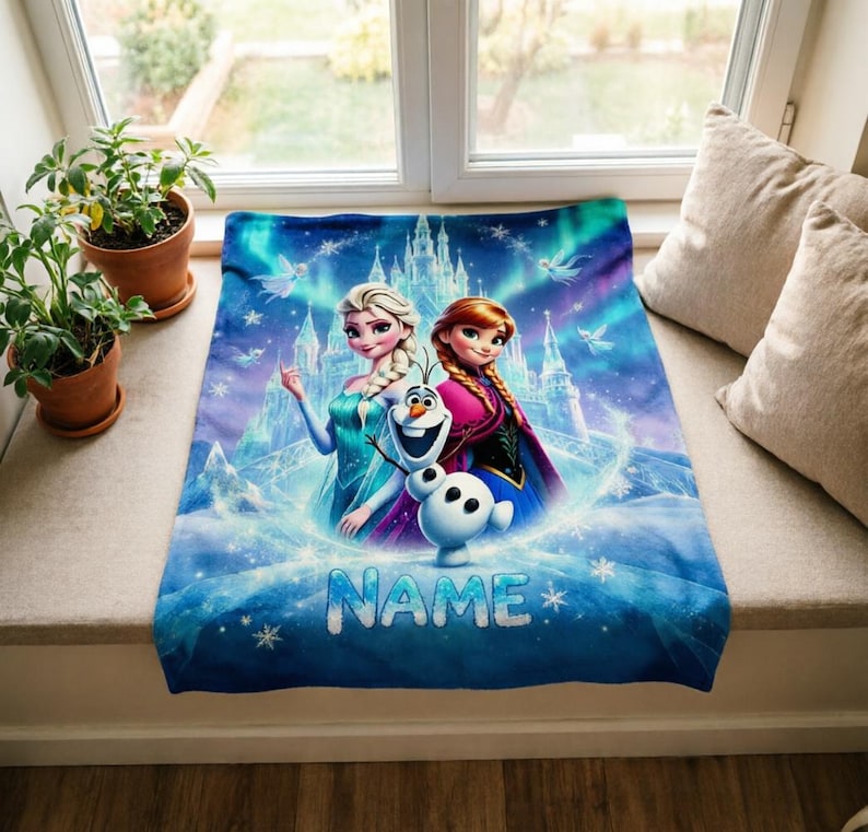 Puede incluir: Una manta rectangular de forro polar con una vibrante escena invernal en azul y morado con Elsa, Anna y Olaf de Frozen. El fondo muestra un castillo de hielo y copos de nieve. La palabra NAME est&aacute; impresa en letras grandes de color azul claro.