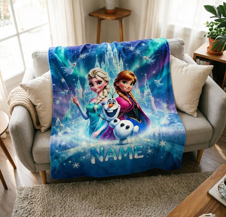 Puede incluir: Una manta de forro polar suave con una vibrante escena azul y morada con Elsa, Anna y Olaf de Frozen. El fondo muestra un castillo helado y copos de nieve. La palabra NAME est&aacute; impresa en letras grandes de color azul claro en el centro.