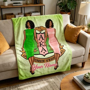 Op de afbeelding: Een lichtgroene deken met twee vrouwen in groene en roze jurken. De deken heeft een wapen met de letters AKA en de woorden "Women Ythp" en "Your Name" in een scriptlettertype.