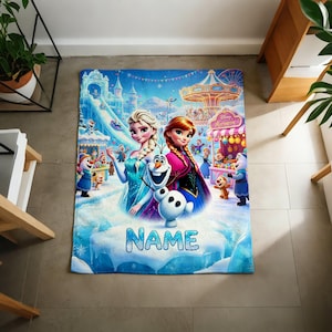 Puede incluir: Una manta rectangular de forro polar con un gr&aacute;fico colorido de Elsa, Anna y Olaf de Frozen en un entorno de feria invernal. El dise&ntilde;o incluye un carrusel, un castillo de hielo y el suelo nevado con la palabra NAME impresa en letras azules.