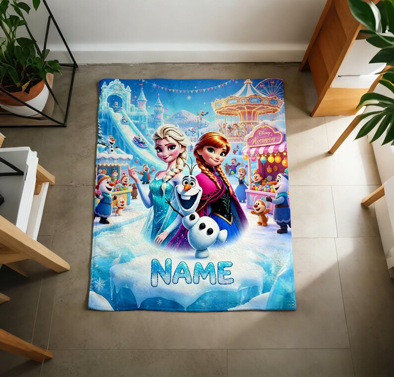 Puede incluir: Una manta rectangular de forro polar con un gr&aacute;fico colorido de Elsa, Anna y Olaf de Frozen en un entorno de feria invernal. El dise&ntilde;o incluye un carrusel, un castillo de hielo y el suelo nevado con la palabra NAME impresa en letras azules.
