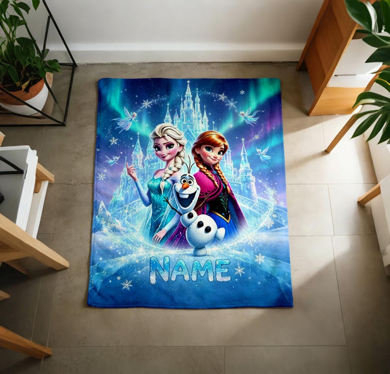 Puede incluir: Una manta rectangular de forro polar con un estampado gr&aacute;fico azul y morado de Elsa, Anna y Olaf de Frozen frente a un castillo de hielo. El dise&ntilde;o incluye copos de nieve, efectos de aurora boreal y la palabra NAME en texto azul.