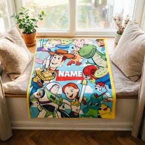 May include: A rectangular fleece blanket featuring a colorful print of various Toy Story characters including Woody, Buzz Lightyear, Jessie, Rex, and the Aliens. The center of the blanket displays a red rectangular graphic with the text NAME.