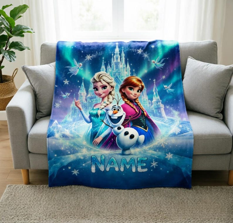 Puede incluir: Una manta rectangular de forro polar con un estampado gr&aacute;fico en azul y morado vibrante de Elsa, Anna y Olaf de Frozen. El dise&ntilde;o incluye un castillo de hielo, copos de nieve y la palabra NAME en letras grandes de color plateado.