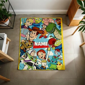 May include: A rectangular fleece blanket with a yellow border featuring a colorful print of various animated characters from the Toy Story franchise, including Woody, Buzz Lightyear, and Jessie, with a red banner in the center displaying the word NAME.
