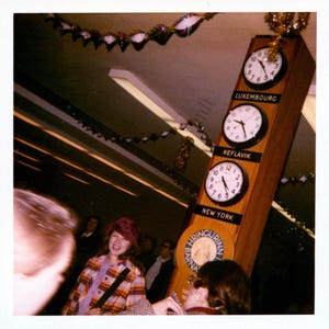 May include: A vertical wooden display board featuring three round analog clocks with black frames and white faces. Each clock is labeled with a black plaque underneath reading Luxembourg, Keflavik, and New York. A circular logo with the text Hringurinn Barnaspitali is visible below the New York clock.