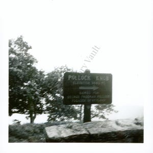 Op de afbeelding: Zwart-witfoto van een bord voor Pollock Knob. Het bord leest "Pollock Knob" met een hoogte van 940 meter. Het bord is gemonteerd op een houten paal en is omgeven door bomen en een bewolkte lucht.