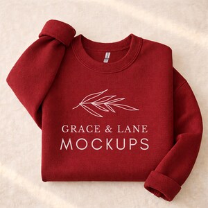 May include: A folded, maroon sweatshirt with the text "GRACE & LANE MOCKUPS" in white, along with a white leaf design. The sleeves are cuffed, and the fabric appears soft.