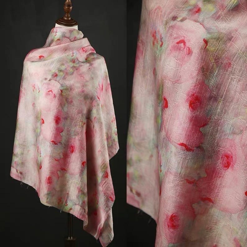 以下が含まれることがあります： ピンク色の花柄のスカーフ。マネキンにドレープされており、デザインが際立っています。生地は、ピンクと赤のバラと緑の葉の、水彩画のようなプリントが施されており、柔らかくロマンチックな美しさを作り出しています。