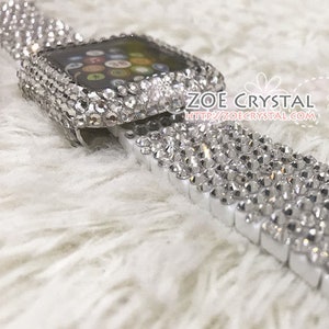 May include: A white Apple Watch band with a clear crystal design. The band is made of metal and has a white background with clear crystals covering the entire surface. The band is designed to fit the Apple Watch.
