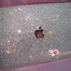 May include: A silver laptop covered in clear rhinestones with the Apple logo in the centre. The laptop has a website address printed on the bottom right corner: "www.zoecrystal.com".
