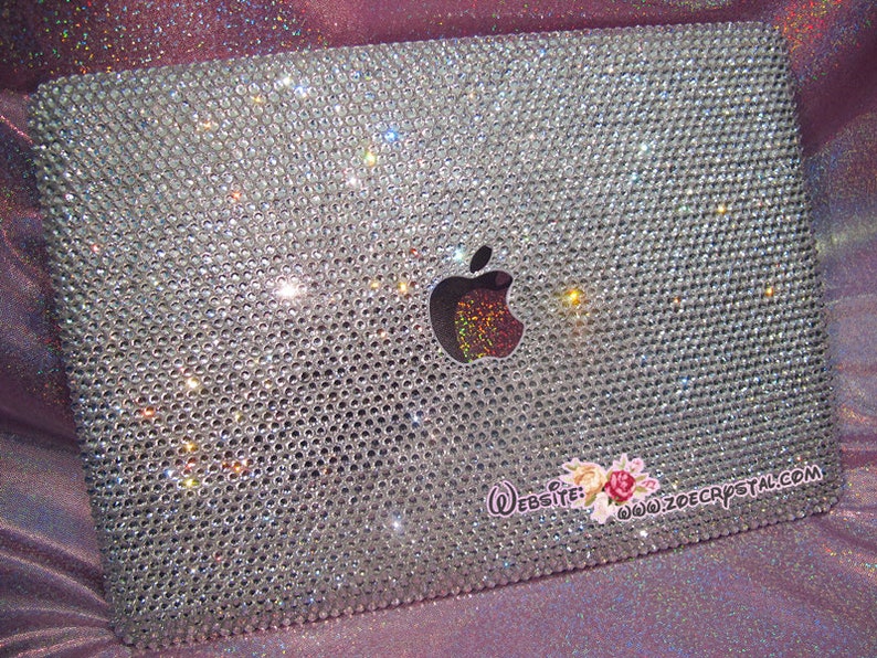 May include: A silver laptop covered in clear rhinestones with the Apple logo in the centre. The laptop has a website address printed on the bottom right corner: "www.zoecrystal.com".