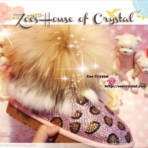 Puede incluir: Botas de piel sintética de leopardo rosa y marrón con un gran pompón de piel esponjosa en la parte superior. Las botas están cubiertas de diamantes de imitación. El texto "Zoe's House of Crystal" está en la parte superior de la imagen. El texto "Zoe Crystal http://zoecrystal.com" está en la parte inferior de la imagen.