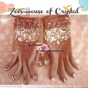 May include: A pair of brown fingerless gloves with a rose-shaped design and embellished with rhinestones. The gloves have a pink and white floral pattern on the back of the hand. The text "Zoe's House of Crystal" is visible at the top of the image.