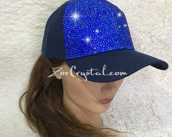 May include: A navy blue baseball cap with a blue rhinestone design on the front. The cap has a mesh back and a curved brim.