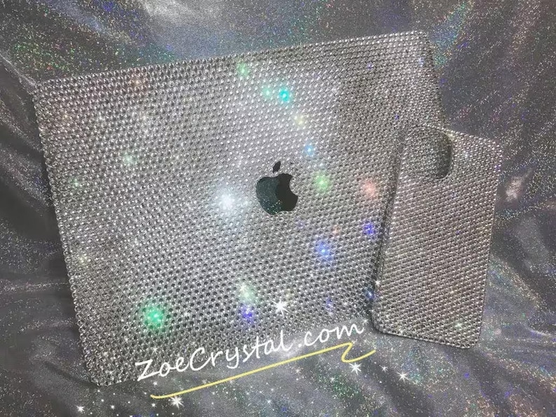 May include: A silver laptop and phone case covered in rhinestones. The laptop has the Apple logo in the centre. The text "ZoeCrystal.com" is visible in the bottom right corner.