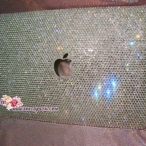 May include: A silver laptop covered in clear rhinestones with an Apple logo in the centre. The laptop is on a pink and purple iridescent background. Website: www.zoecrystal.com