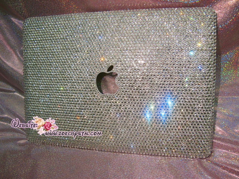 May include: A silver laptop covered in clear rhinestones with an Apple logo in the centre. The laptop is on a pink and purple iridescent background. Website: www.zoecrystal.com