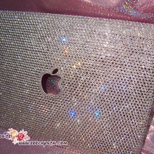 May include: A silver laptop covered in clear rhinestones with an Apple logo in the centre. The laptop is on a pink sparkly background. The website www.zdecrystal.com is visible in the bottom right corner.
