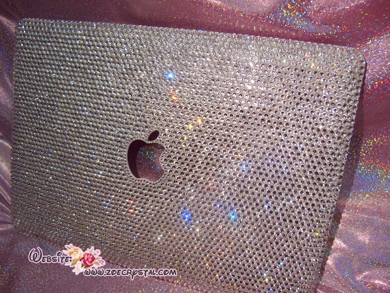 May include: A silver laptop covered in clear rhinestones with an Apple logo in the centre. The laptop is on a pink sparkly background. The website www.zdecrystal.com is visible in the bottom right corner.