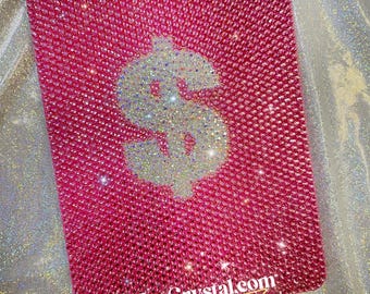May include: A rectangular, hot pink, crystal-covered item with a large, sparkling dollar sign in the center. The surface is densely packed with small crystals. The text "ZoeCrystal.com" is at the bottom.