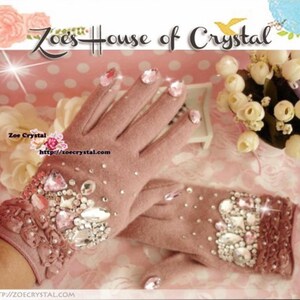 May include: A pair of pink fingerless gloves with a lace cuff and a large cluster of rhinestones on the back of the hand. The gloves are decorated with pink and clear rhinestones. The text "Zoe's House of Crystal" is visible in the background.