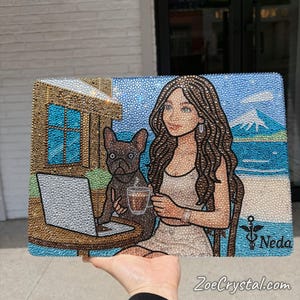 May include: A rectangular, bedazzled artwork featuring a woman, a dog, and a laptop at a table. The artwork depicts a beach scene with a mountain in the background. The woman is holding a cup, and the dog is sitting next to her. The artwork has the text "Neda" and "ZoeCrystal.com".