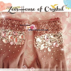 May include: A pair of pink fingerless gloves with a floral design and crystal embellishments. The gloves are made of a soft, fuzzy material. The text "Zoe's House of Crystal" and "Zoe Crystal" is visible on the image. The website address "http://zoecrystal.com" is also visible.